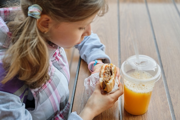 Gros Plan De La Main De L'enfant Manger Un Hamburger Et Boire Du Jus D'orange