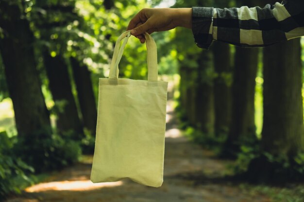 Gros plan d'une main féminine méconnaissable tenant un sac écologique en coton dans le parc Sac écologique réutilisable dans le parc Maquette Mode de vie durable Sans plastique zéro déchet sans vie Passez au vert