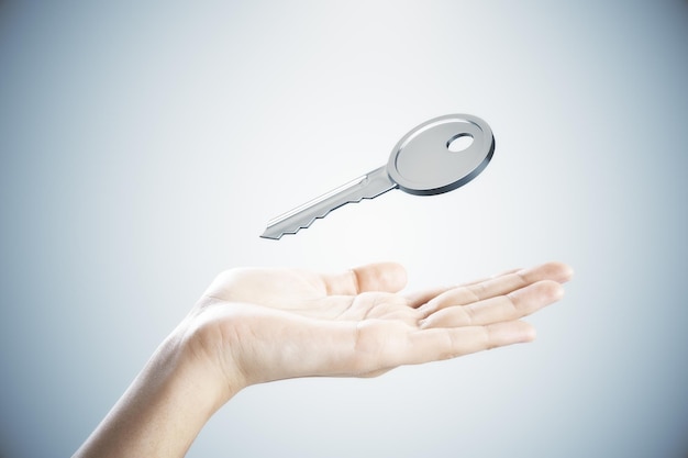 Photo gros plan sur une main féminine tenant une clé en argent sur fond gris concept d'hypothèque et d'achat
