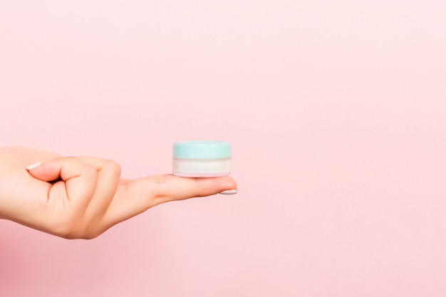 Gros plan de la main féminine tenant un pot de cosmétiques sur fond rose