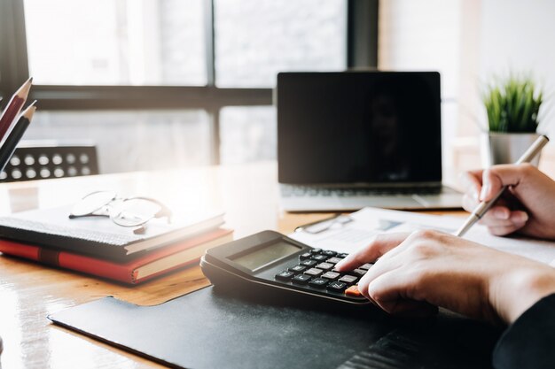 Gros plan d'une main de femme d'affaires ou de comptable tenant un stylo travaillant sur une calculatrice pour calculer des données commerciales