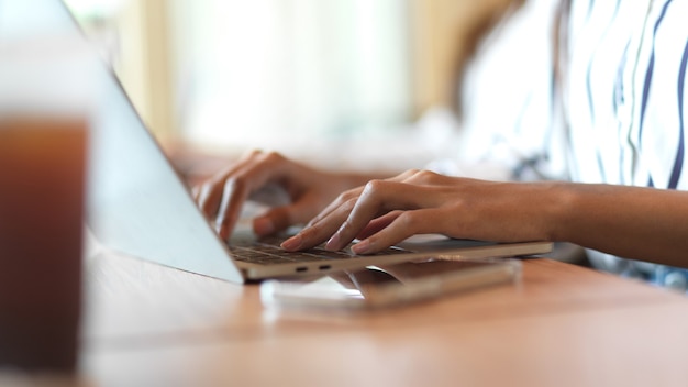 Gros plan sur la main d'une femme d'affaires tapant sur un clavier d'ordinateur portable sur le bureau en bois dans la salle de bureau