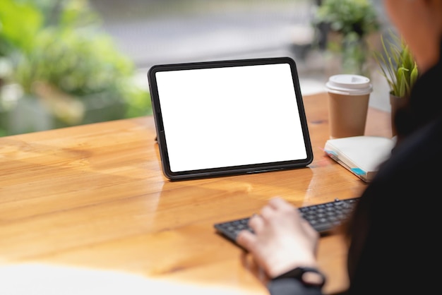 Gros plan sur une main de femme à l'aide d'un écran blanc vide de tablette d'ordinateur sur le bureau.