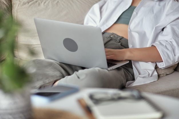 Gros plan main de femme à l'aide d'un ordinateur portable assis sur un canapé à la maison travail à distance à la maison