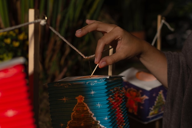 Gros plan d'une main de femme allumant une bougie à l'intérieur d'une lanterne en papier colorée