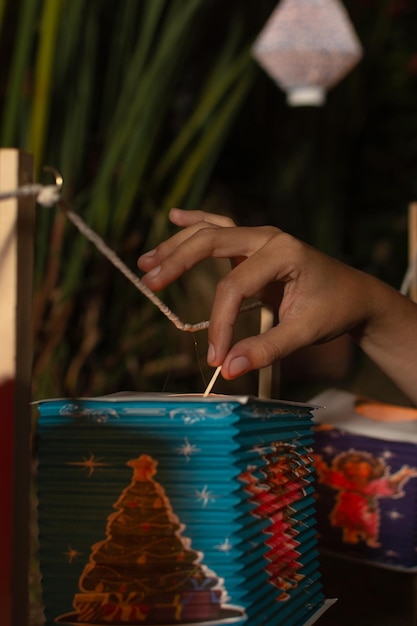 Gros plan d'une main de femme allumant une bougie à l'intérieur d'une lanterne en papier colorée