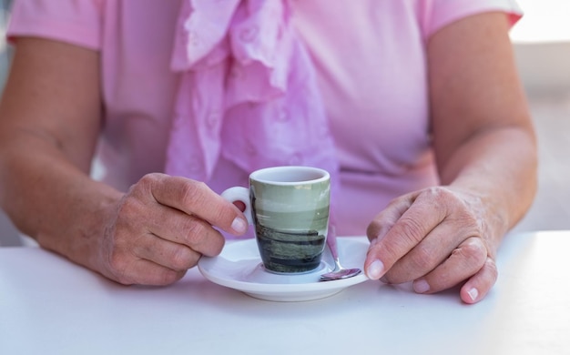 Gros plan sur une main de femme caucasienne tenant une tasse de café assise à une table blanche