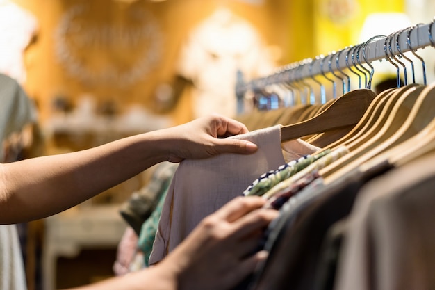 Photo gros plan d'une main de femme, choisissant des vêtements d'occasion jeunes et discount t-shirt en magasin
