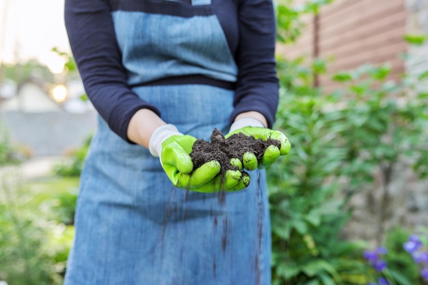 Gros plan sur la main d'une femme dans des gants de jardinage avec un sol fertile noir