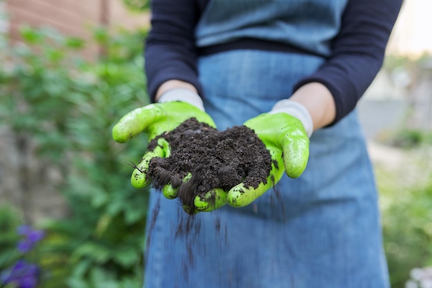 Gros plan sur la main d'une femme dans des gants de jardinage avec un sol fertile noir