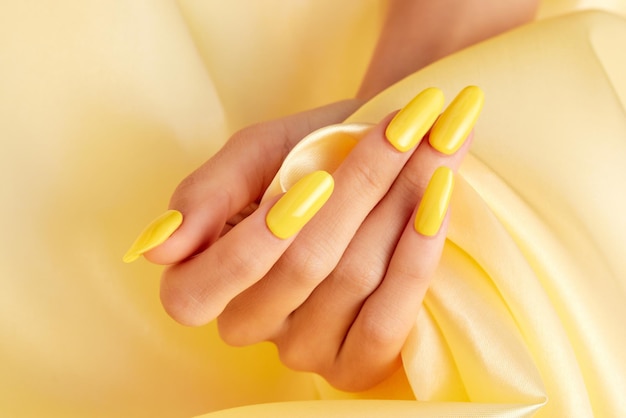 Gros plan de la main d'une femme avec du vernis à ongles jaune sur un tissu de soie jaune