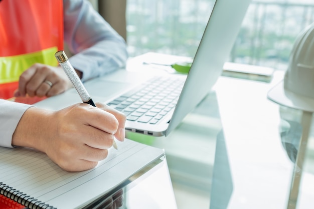 Gros plan main femme ingénieur écrit note sur son cahier au site de contruction.