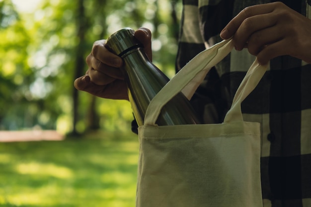 Photo gros plan d'une main de femme méconnaissable tenant une bouteille d'eau d'un sac écologique thermo eau en acier réutilisable