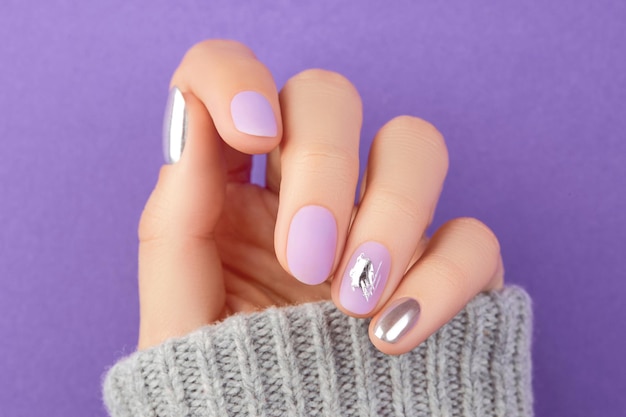 Gros plan sur la main d'une femme avec un motif d'ongles lavande mat sur fond violet