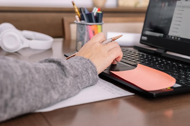 Gros plan d'une main de femme prenant des notes devant un ordinateur