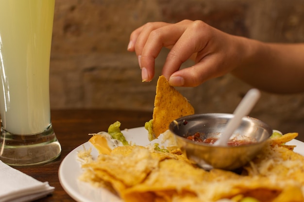 Gros plan d'une main de femme saisissant une tortilla à partir d'une assiette de nachos
