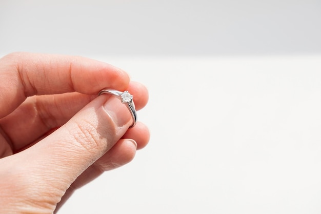 Gros plan sur une main de femme tenant une bague élégante sur fond blanc Bague brillante de fiançailles en diamant