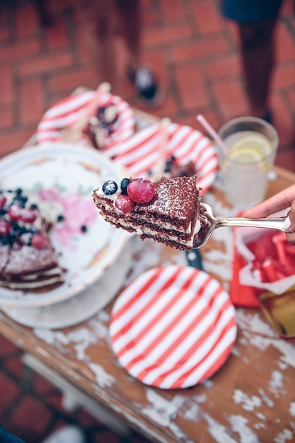 Gros plan d'une main de femme tenant un morceau de gâteau au chocolat nu avec de la crème et des baies dans un serveur