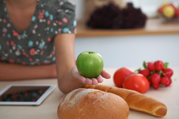 Gros plan sur une main de femme tenant une pomme verte dans l'intérieur de la cuisine De nombreux légumes et autres repas à la table en verre sont prêts à être cuits bientôt