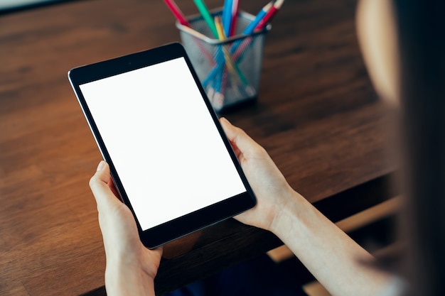 Gros plan d'une main de femme tenant une tablette numérique sur la table et l'écran est vide.