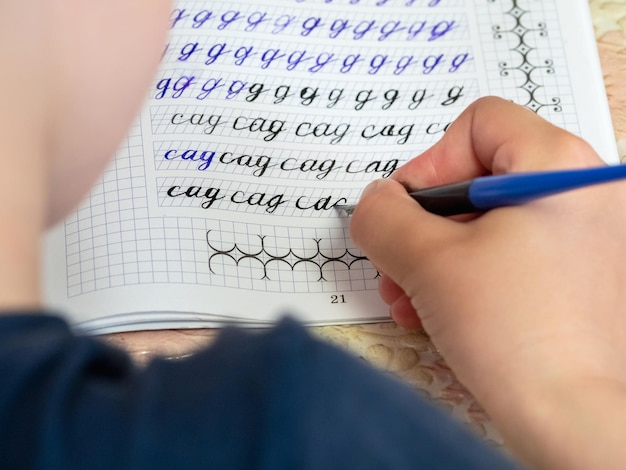 Gros plan de la main d'une fille avec un stylo écrivant des mots russes à la main sur du papier bloc-notes blanc traditionnel La fille écrit sa première lettre en russe