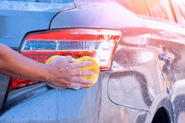 Gros plan sur la main de l'homme à l'aide d'une éponge et de mousse pour laver la voiture moderne des feux arrière