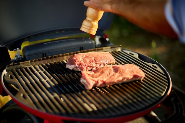 Gros Plan Sur La Main De L'homme Assaisonnant La Viande Sur Le Gril à Gaz Sur Le Barbecue En Plein Air