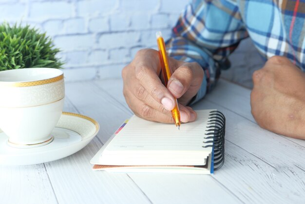 Gros plan de la main de l'homme écrit sur le bloc-notes.