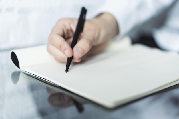 Gros plan sur une main d'homme écrivant dans un journal intime sur une table en verre concentré sur une main avec un stylo