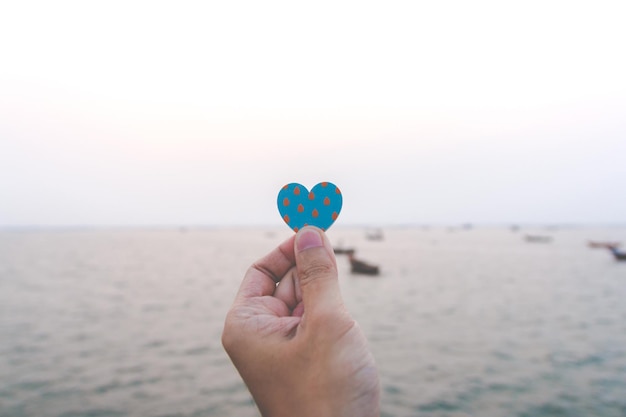 Gros plan de main homme tenant un coeur de papier avec le fond de la mer. concept d'amour, bonne Saint-Valentin.