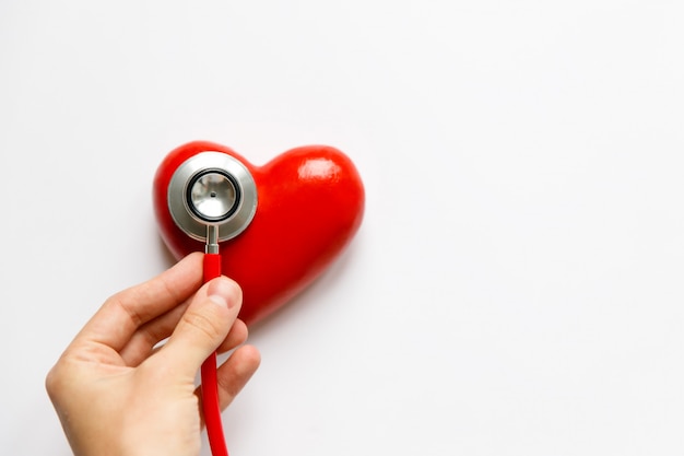 Gros plan de la main de l'homme tenant un stéthoscope rouge sur le cœur - dispositif de diagnostic médical pour l'auscultation (écoute) des sons provenant du cœur