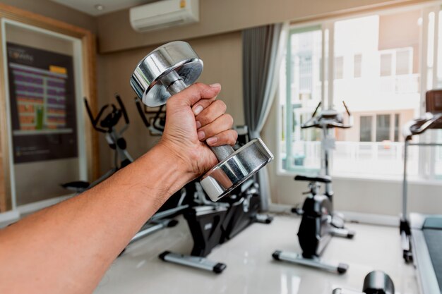 Gros plan la main d'un homme tient un haltère avec sa main gauche dans la salle de gym, Concept pour l'exercice et les soins de santé.