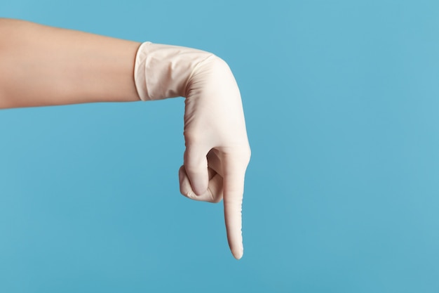 Photo gros plan de la main humaine dans des gants chirurgicaux blancs montrant ou pointant vers le bas avec le doigt.