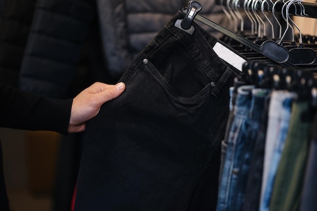 Gros plan sur une main humaine prenant un pantalon jeans noir pour homme