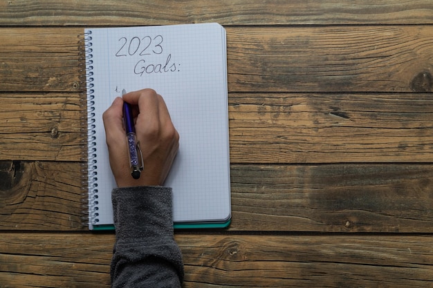 Gros plan d'une main de jeune femme écrivant dans un cahier les résolutions du Nouvel An pour 2023 avec espace de copie