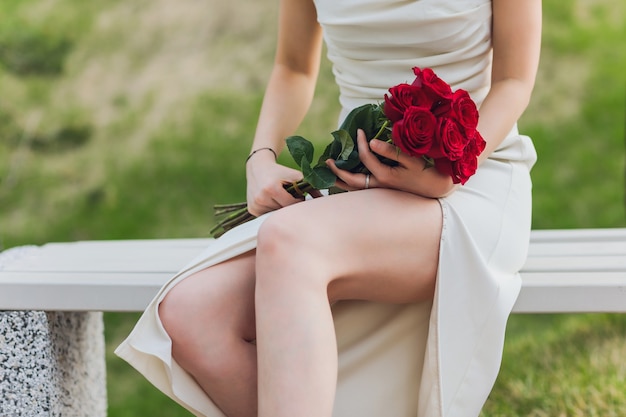 Gros plan de la main de la jeune femme tenant des fleurs roses rouges sur fond extérieur.