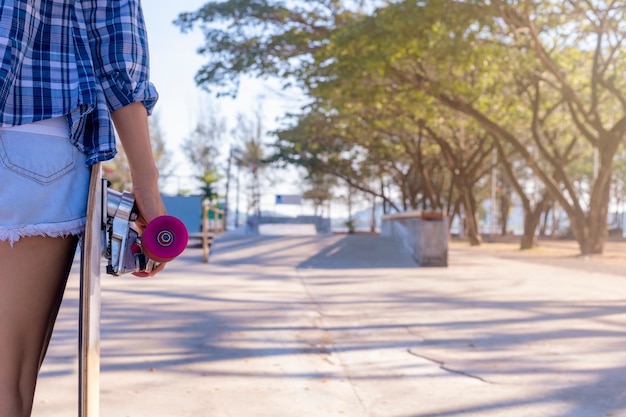 Gros plan sur la main de la jeune femme tenant une planche à roulettes sur le parc public de rampe de skate.