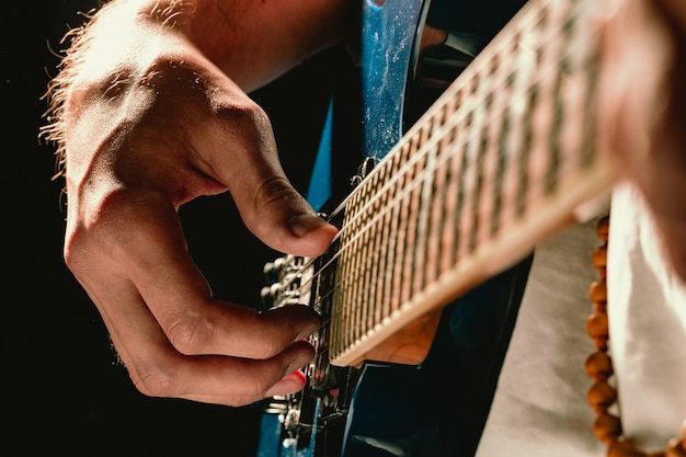 Gros plan de la main masculine jouant de la guitare électrique dans l'obscurité