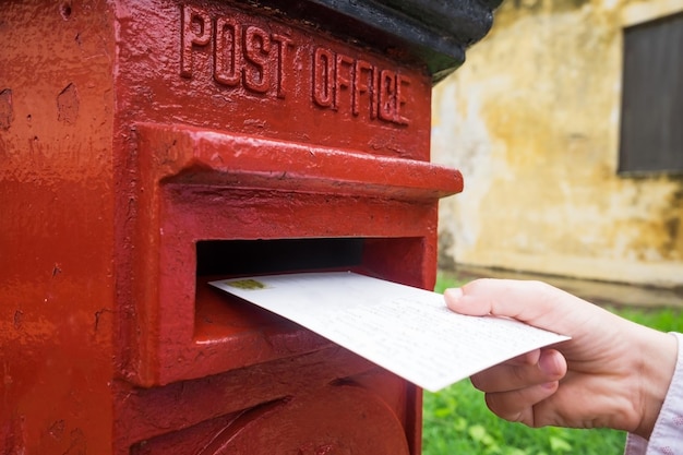 Gros plan sur une main masculine mettant une lettre dans une boîte aux lettres rouge Concept de type de communication vintage