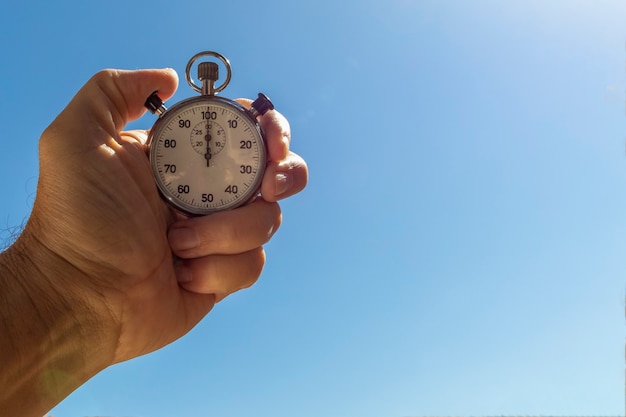 Gros plan d'une main masculine tenant un chronomètre analogique sur fond bleu. Concept de gestion du temps.