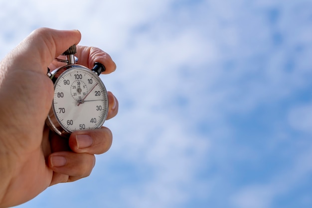 Gros plan d'une main masculine tenant un chronomètre analogique sur fond bleu. Concept de gestion du temps.