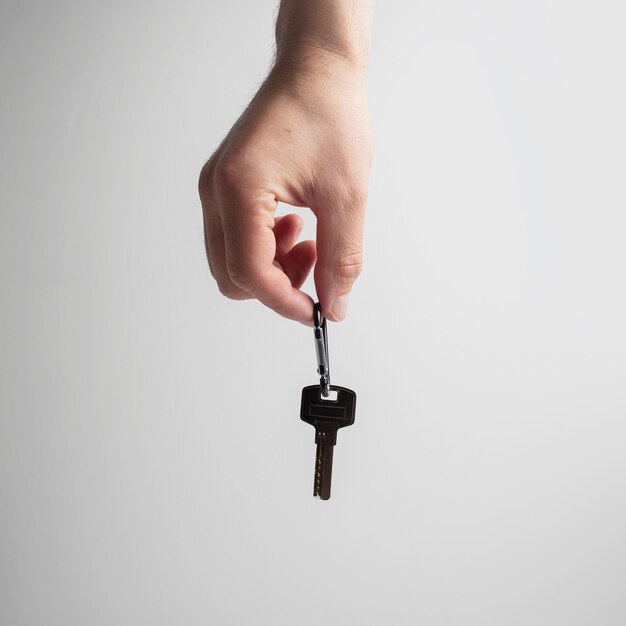 Gros plan d'une main masculine tenant une clé de la maison sur blanc.