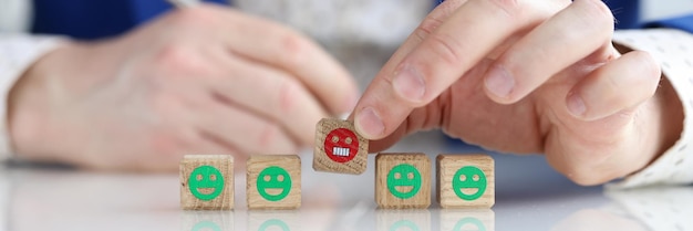 Gros plan d'une main masculine tenant des cubes en bois avec un homme emoji en colère donnant un service de rétroaction négative