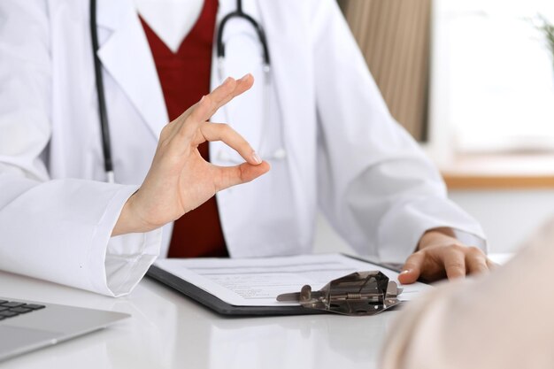 Gros plan sur la main d'un médecin montrant un signe ok pendant que le médecin et son patient discutent des dossiers médicaux après un examen médical.