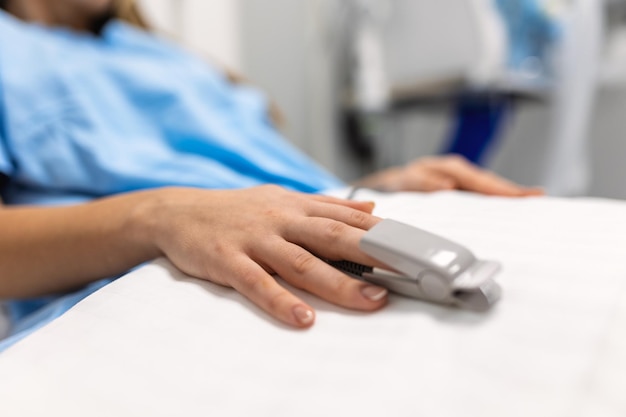 Gros plan de la main avec oxymètre de pouls au doigt Utilisation de l'oxymètre de pouls au doigt surveillance des signes vitaux Concept médical Chambre à coucher ou chambre d'hôpital pour jeune patient