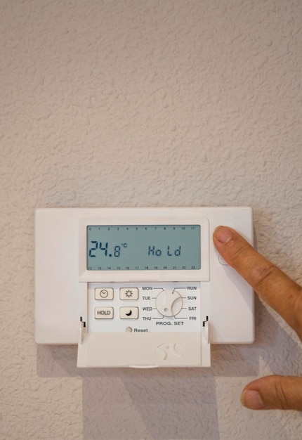 Gros plan de la main de la personne réglant la température sur le thermostat numérique à la maison attaché à l'espace de copie du mur