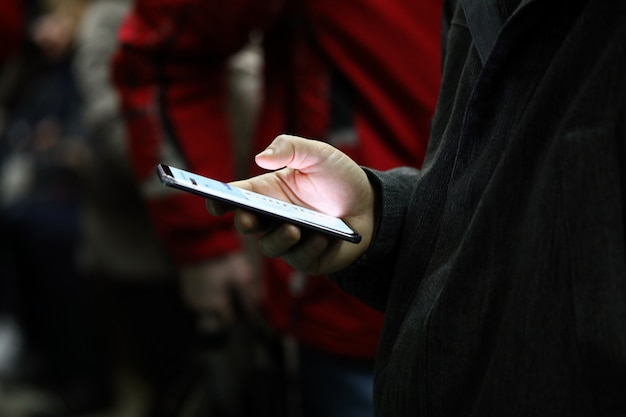 Gros plan de la main des personnes tenant un téléphone mobile avec écran lumineux. Man défilement des nouvelles ou jouer au jeu. Tuez le temps et le divertissement dans le concept de transport public