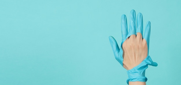 Gros plan sur la main Porter des gants médicaux déchirés ou des gants en caoutchouc déchirés sur fond de couleur bleu et vert ou bleu Tiffany.coclor monotone.