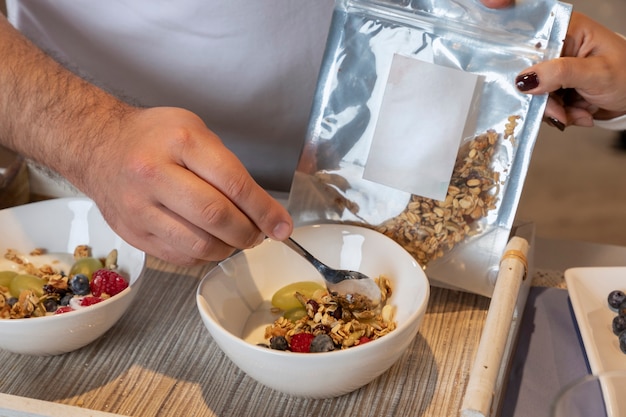 Gros plan sur la main se déplaçant avec une cuillère un bol avec du granola au yaourt et des fruits