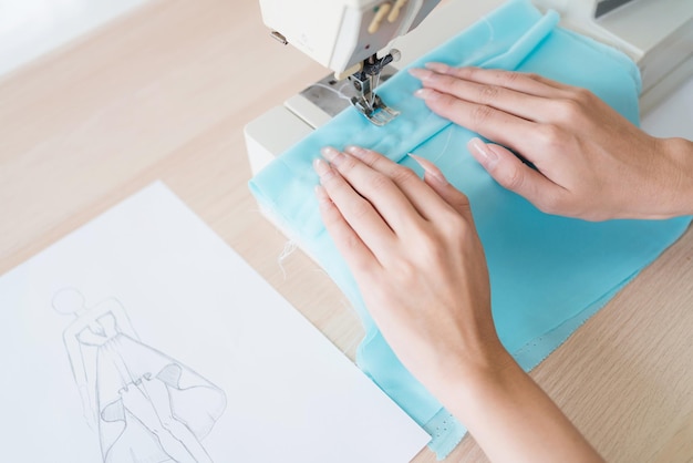 Gros plan main de tailleur femme cousant des vêtements avec une machine à coudre Une jeune créatrice de mode féminine séduisante sourit et regarde la caméra avec un portant à vêtements en arrière-plan en studio